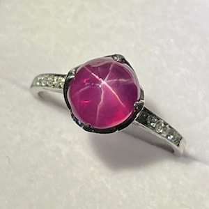 May include: A silver ring with a pink star ruby gemstone and a band of small diamonds.