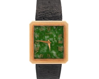 May include: A gold-toned rectangular Piaget watch with a green jade face and gold hands. The watch has Roman numerals and a black leather band. The watch face is approximately 1 inch square.