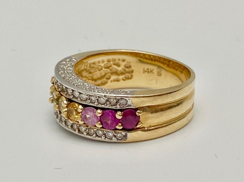 May include: A gold band ring with a row of colorful gemstones and a row of diamonds. The ring is marked "14K" on the inside.