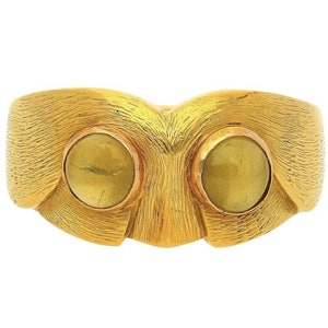 May include: A gold ring with two large, round, yellow gemstones set into the band. The ring has a textured, brushed finish.