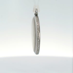 May include: A silver pendant with a round shape and a single row of small diamonds around the edge.