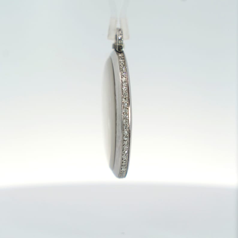 May include: A silver pendant with a round shape and a single row of small diamonds around the edge.
