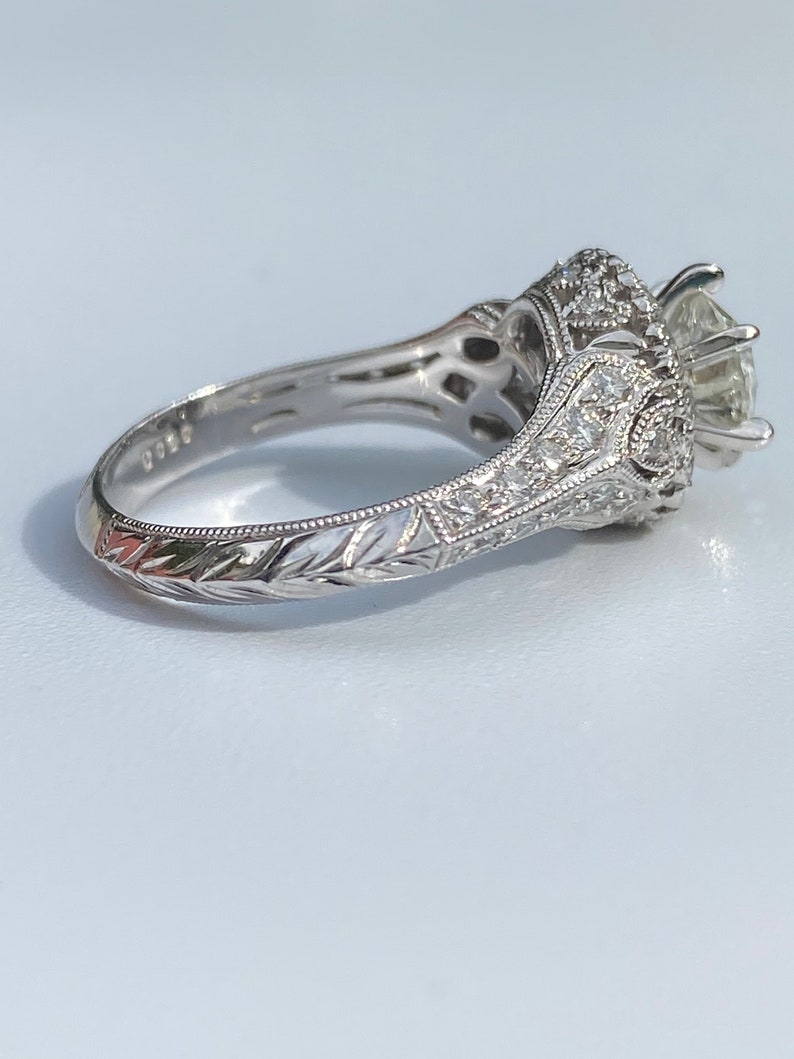 May include: A silver engagement ring with a large center diamond and smaller diamonds set in a halo around it. The band is engraved with a floral design.
