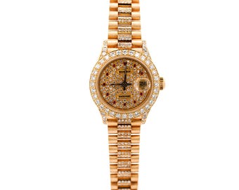 May include: A gold-toned wristwatch with a round face and a matching band. The watch face is covered in small, sparkling stones, with a date display at the 3 o'clock position. The bezel and band are also adorned with gemstones.