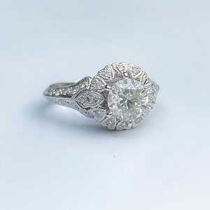 May include: A silver engagement ring with a large round diamond surrounded by smaller diamonds in a floral design.