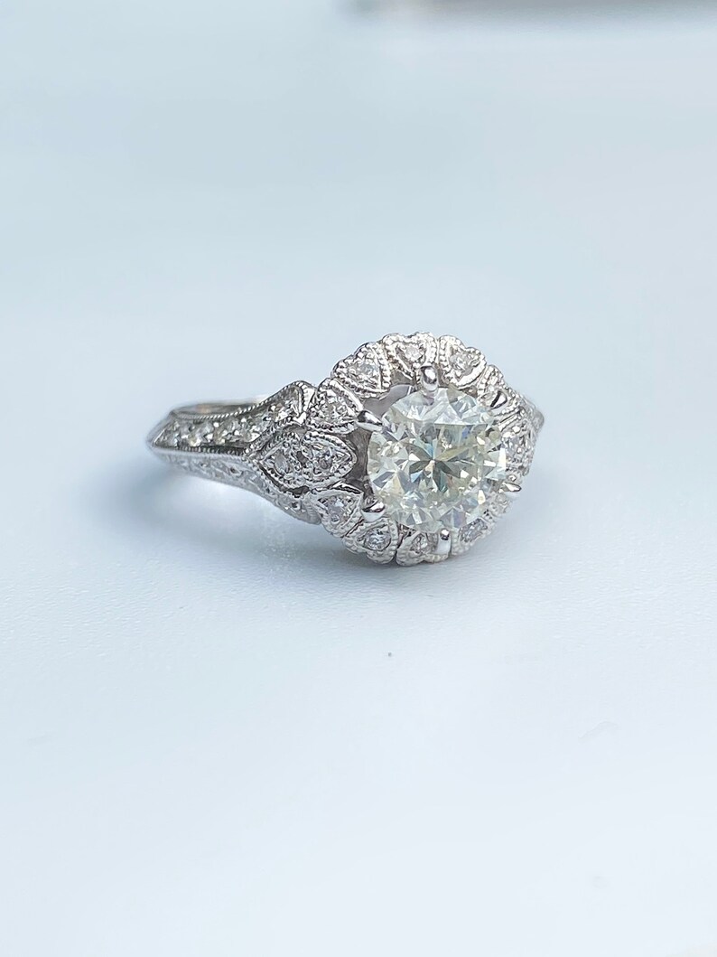 May include: A silver engagement ring with a large round diamond surrounded by smaller diamonds in a floral design.