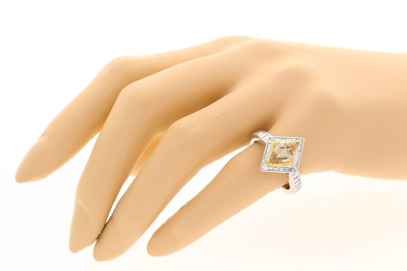 May include: A white gold ring featuring a square-shaped yellow diamond set within a halo of smaller diamonds.