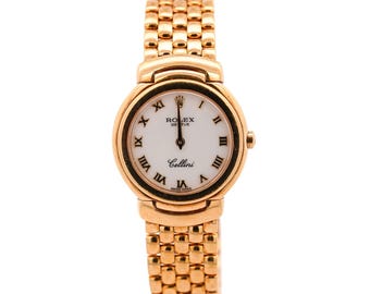May include: A gold-toned Rolex Cellini wristwatch with a white face and black Roman numerals. The watch has a round face and a linked band. The watch face displays the Rolex logo and the word "Cellini".