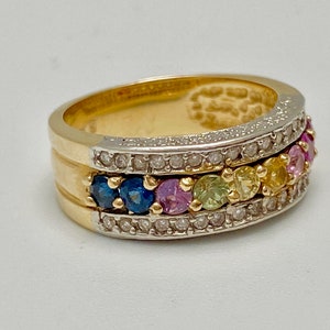 May include: A gold band ring with a row of colorful gemstones set in a white metal band. The gemstones are surrounded by smaller diamonds.