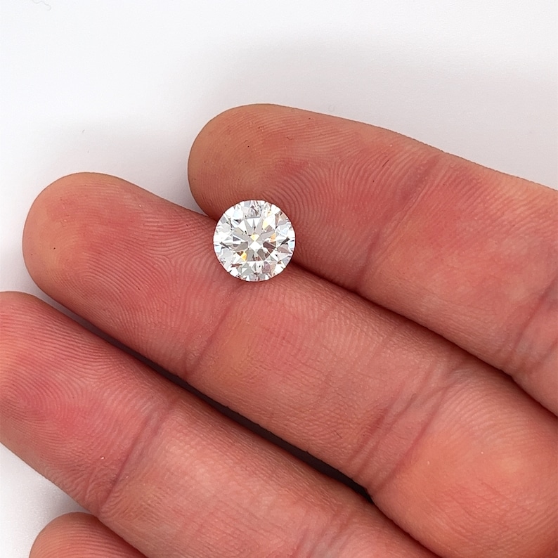 May include: A clear round diamond gemstone held in a hand.