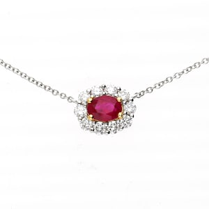 May include: A fine necklace with a vivid red oval ruby gemstone, encircled by a halo of brilliant white diamonds. The pendant is set in a gold and silver setting, suspended from a delicate silver chain. A classic piece of jewellery.