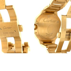 May include: A gold Cartier watch with a round face and a gold metal strap. The watch has a date window and the words 'Cartier' and 'Swiss Made' are engraved on the back.