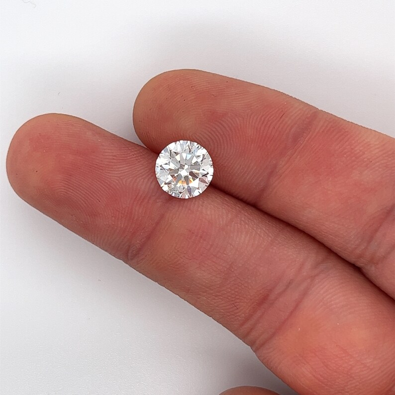 May include: A clear round diamond gemstone on a finger.