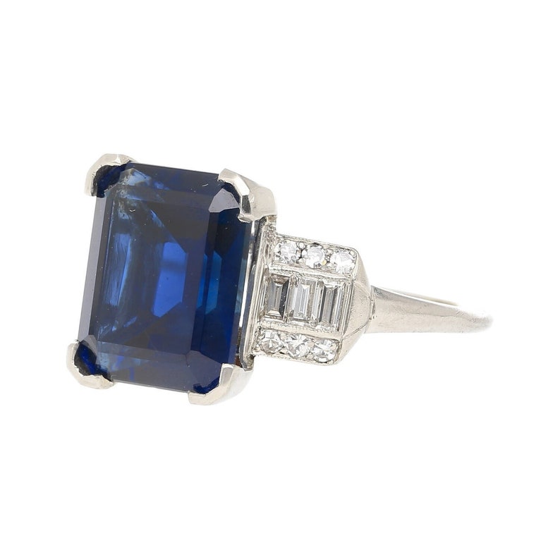K&ouml;nnte beinhalten: Ein Platinring mit einem gro&szlig;en, tiefblauen Smaragdschliff-Saphir und kleineren Diamanten, die in Pav&eacute;-Fassung gefasst sind.