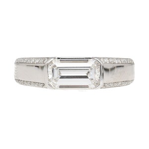 May include: A silver ring with a large, clear emerald-cut diamond set in the center. The band is decorated with smaller diamonds.