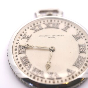 May include: A silver pocket watch with a white face and diamond-encrusted Roman numeral hour markers. The watch face also features the text "VACHERON & CONSTANTIN GENEVE".