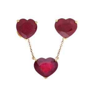 Puede incluir: Un collar de oro con tres colgantes de rubí en forma de corazón. Los colgantes de rubí son de color rojo intenso y están conectados por delicadas cadenas de oro. El collar tiene un diseño clásico y elegante.