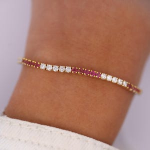 Pode incluir: Um bracelete de ténis de ouro com pedras redondas de rubi e diamantes alternadas.