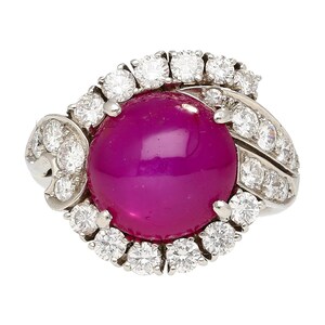 May include: A ring featuring a large, cabochon-cut ruby encircled by a halo of smaller diamonds. The ring is set in platinum and has a delicate, floral design.