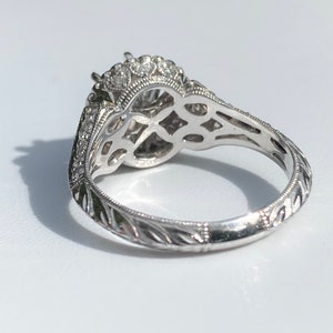 May include: A silver engagement ring with a large center stone surrounded by smaller stones. The band is engraved with a delicate floral pattern.