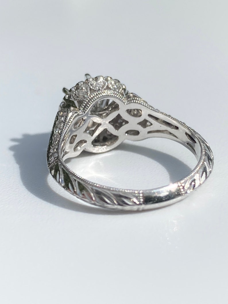 May include: A silver engagement ring with a large center stone surrounded by smaller stones. The band is engraved with a delicate floral pattern.