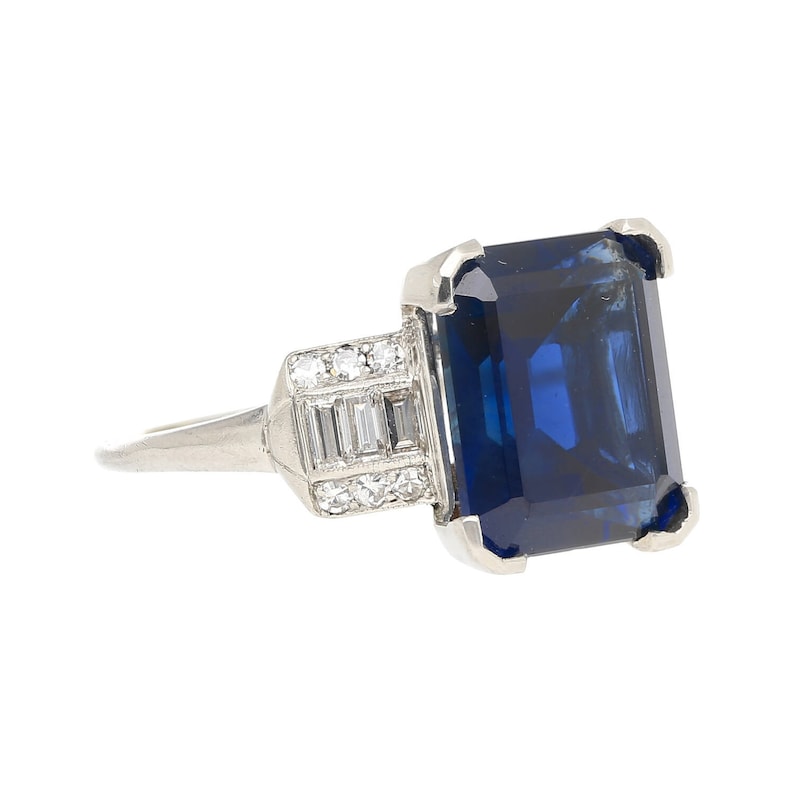 K&ouml;nnte beinhalten: Ein Platinring mit einem gro&szlig;en, tiefblauen Smaragdschliff-Saphir und einer Reihe kleinerer Diamanten, die in Pav&eacute;-Fassung gefasst sind.