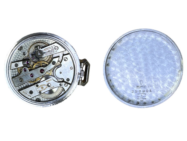 May include: A silver pocket watch with a detailed view of the inner workings of the watch movement. The back of the watch is engraved with the words "Platine" and the number "256991".