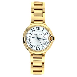 May include: A gold-tone Cartier Ballon Bleu watch with a white dial and Roman numeral hour markers. The watch has a round case and a gold-tone bracelet.