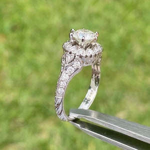 May include: A silver engagement ring with a large, round, clear diamond center stone. The ring has a delicate, intricate design with smaller diamonds set around the center stone and along the band.