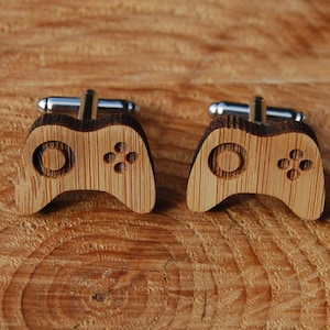 May include: A pair of wooden cufflinks shaped like a video game controller. The cufflinks are made of dark brown wood and have a silver metal clasp.