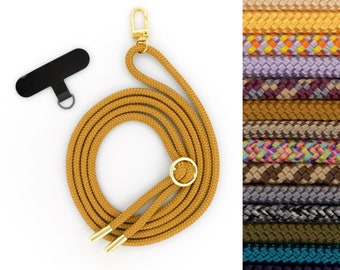 May include: A mustard yellow rope camera strap with a gold metal ring and a gold metal clip. The strap is coiled and laid flat on a white surface. A black plastic camera strap clip is also shown.