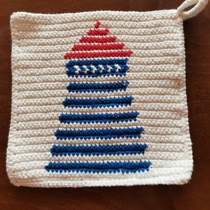 Könnte beinhalten: Ein quadratischer, cremefarbener Topflappen aus Häkelarbeit mit einem Leuchtturm-Design. Der Leuchtturm ist in Rot und Blau auf weißem Hintergrund dargestellt. Eine kleine Schlaufe ist zum Aufhängen an einer Ecke befestigt.