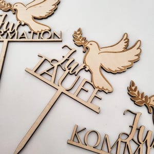 Könnte beinhalten: Holz-Kuchentopper mit einer Taube, die einen Olivenzweig hält, und dem Text "für Taufe" in Kursivschrift.