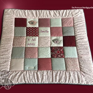 Könnte beinhalten: Eine rosa-grüne Patchwork-Babydecke mit einem Teddybär-Applikationen und dem Namen "Smilla" bestickt. Die Decke hat auch das Datum "8. Juli 2021" bestickt.