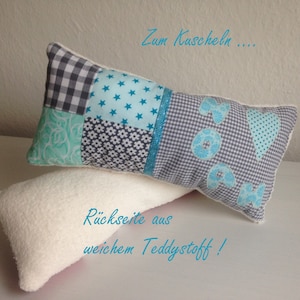 Könnte beinhalten: Ein graues und blaues Patchwork-Kissen mit dem Wort "Mama" in blauen Stoffbuchstaben. Das Kissen hat auf der einen Seite ein Herz und auf der anderen Seite den Text "Zum Kuscheln...". Die Rückseite des Kissens ist aus weichem Teddystoff. Der Text "Rückseite aus weichem Teddystoff!" ist auf dem Kissen geschrieben.