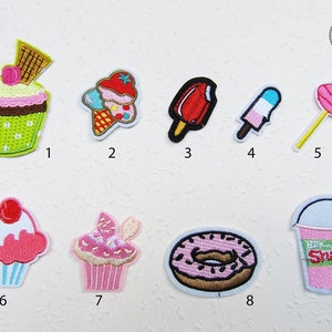 Könnte beinhalten: Neun gestickte Bügelbilder mit verschiedenen süßen Leckereien, darunter Cupcakes, Eiswaffeln, Eis am Stiel, Lutscher und einen Milchshake. Die Patches sind bunt und verspielt und perfekt, um jedem Projekt eine süße Note zu verleihen.