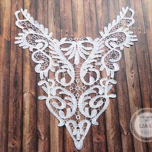 Könnte beinhalten: Weiße Spitzenborte mit einem zarten Blumenmuster. Die Borte ist V-förmig und hat eine spitze Unterseite. Sie ist perfekt, um jedem Kleidungsstück einen Hauch von Eleganz zu verleihen.