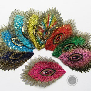 Könnte beinhalten: Sortiment aus bunten, federförmigen Stoff-Patches in Form von Pfauenfedern mit goldenen Pailletten und Stickereien. Die Patches sind fächerförmig angeordnet.