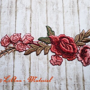 Könnte beinhalten: Eine rote und rosafarbene gestickte Blumenapplikation mit grünen Blättern. Die Applikation zeigt eine große Rose mit kleineren Rosen und Blättern.