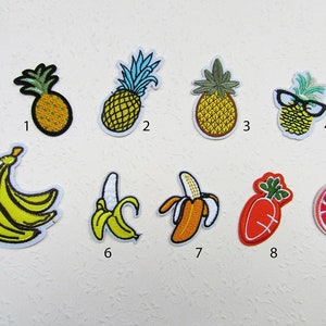 Könnte beinhalten: Neun gestickte Bügelbilder mit verschiedenen Früchten, darunter Ananas, Bananen, Karotten und Orangen. Die Patches sind farbenfroh und detailliert, mit einer Vielzahl von Texturen und Mustern.