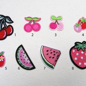 Könnte beinhalten: Acht gestickte Bügelbilder mit verschiedenen Früchten, darunter Kirschen, Erdbeeren, Wassermelonen und Äpfel. Die Patches sind in Rot-, Rosa-, Grün- und Weißtönen gehalten.