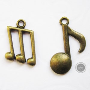Könnte beinhalten: Zwei antike goldfarbene Metall-Musiknoten-Anhänger. Ein Anhänger ist ein Violinschlüssel und der andere eine einzelne Note.