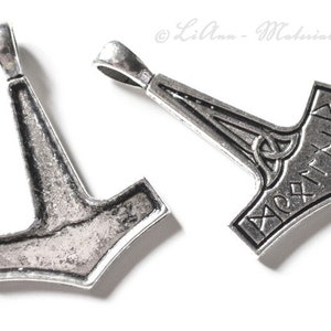 Könnte beinhalten: Zwei silberne Mjolnir-Anhänger, einer mit einem detaillierten Design und der andere mit einer glatten Oberfläche. Beide Anhänger haben eine Öse oben zum Anbringen an einer Kette.