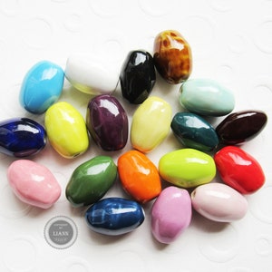 Könnte beinhalten: Eine Sammlung von 20 bunten ovalen Keramikperlen. Die Perlen sind in verschiedenen Farbtönen von Blau, Grün, Gelb, Rot, Rosa, Lila, Braun und Weiß.