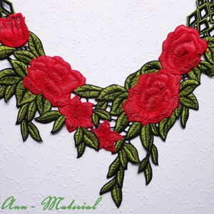 Könnte beinhalten: Rote gestickte Blumenspitze mit grünen Blättern und schwarzem Hintergrund. Die Spitze hat ein sich wiederholendes Muster aus Rosen und Blättern.
