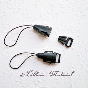 Könnte beinhalten: Zwei schwarze Kunststoff-Lanyard-Clips mit schwarzen Schnurläufen. Ein Clip ist eine einfache Schnalle, der andere ist ein Drehclip.