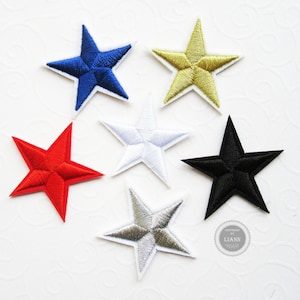 Könnte beinhalten: Sechs gestickte Stern-Patches in verschiedenen Farben, darunter Rot, Blau, Gold, Weiß, Silber und Schwarz. Die Sterne sind alle gleich groß und gleich geformt und in einem Halbkreis auf weißem Hintergrund angeordnet.