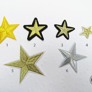 Könnte beinhalten: Sechs goldene und silberne, sternförmige Bügelbilder. Die Sterne sind unterschiedlich groß und haben verschiedene Umrisse. Die Patches sind von 1 bis 6 nummeriert.