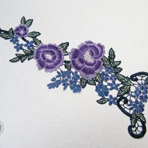 Könnte beinhalten: Lila und blaue gestickte florale Spitzenborte mit einem zarten Design. Die Borte zeigt große und kleine Blumen, Blätter und komplizierte Details.