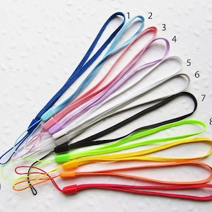 Könnte beinhalten: Eine Sammlung von elf farbigen Handschlaufen in verschiedenen Farbtönen, darunter Blau, Rosa, Lila, Grau, Schwarz, Grün, Gelb, Orange und Rot. Jeder Riemen hat eine Schlaufe und einen Kunststoffverbinder.